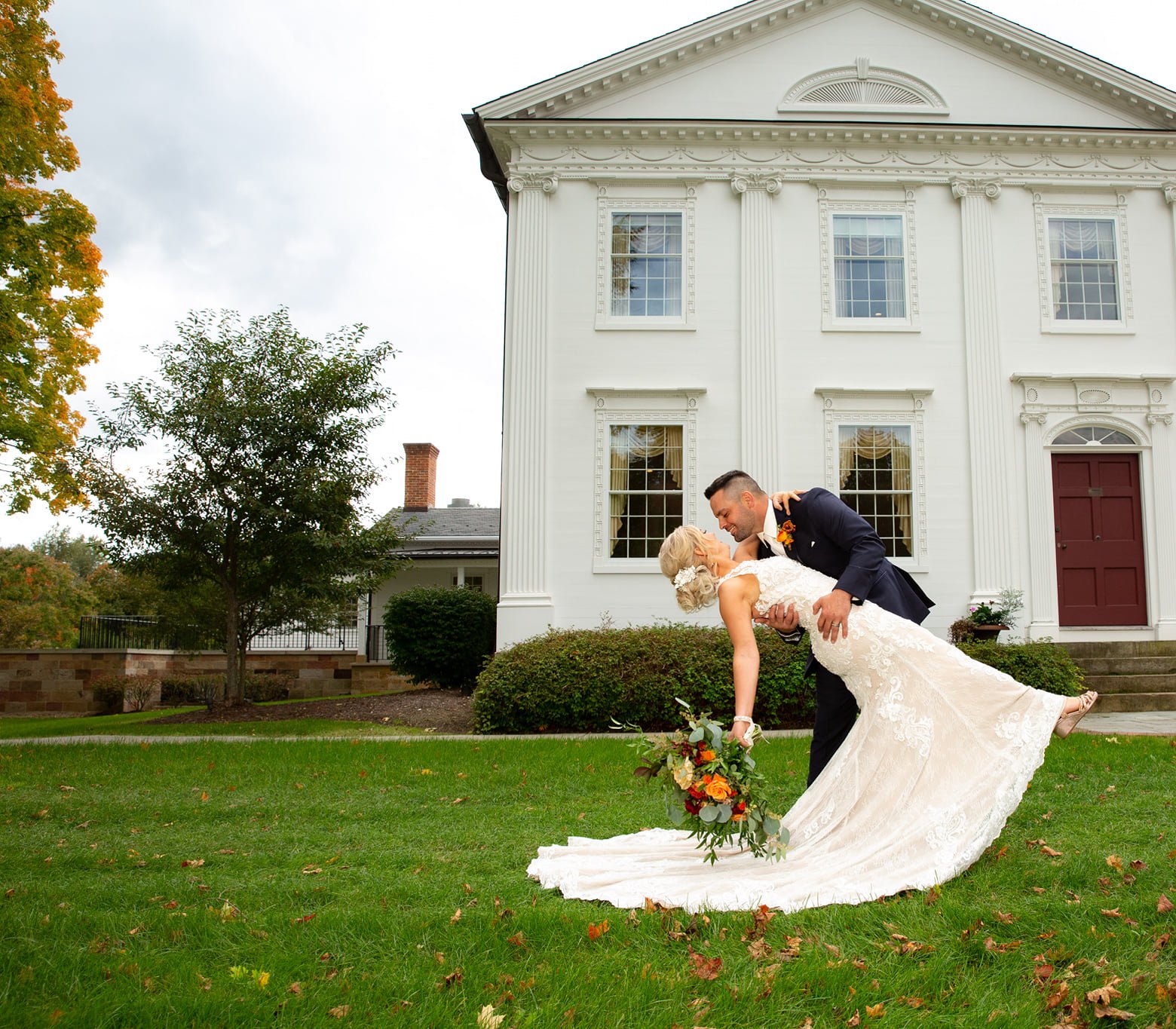 Bride and groom dip on the lawn in front of a white historic wedding venue